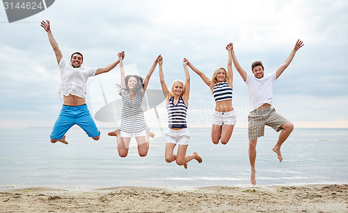 Image of smiling friends in sunglasses walking on beach