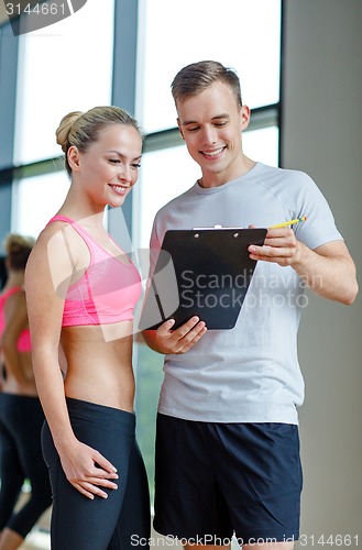 Image of smiling young woman with personal trainer in gym