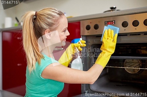 Image of happy woman cleaning cooker at home kitchen