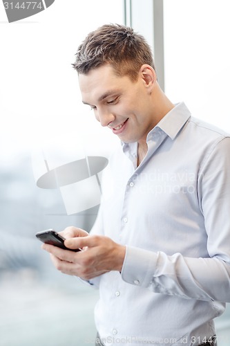 Image of smiling businessman with smartphone in office