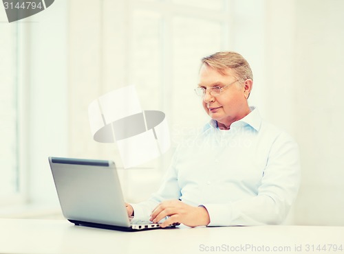 Image of old man in eyeglasses working with laptop at home