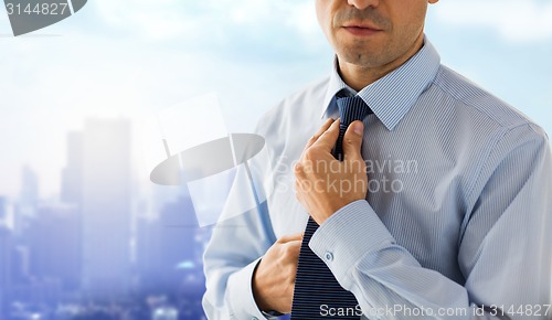 Image of close up of man in shirt adjusting tie on neck