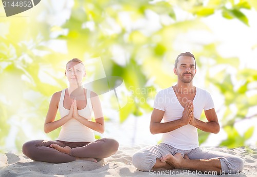 Image of smiling couple making yoga exercises outdoors