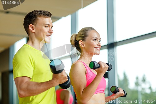 Image of smiling man and woman with dumbbells in gym