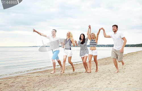 Image of smiling friends in sunglasses running on beach