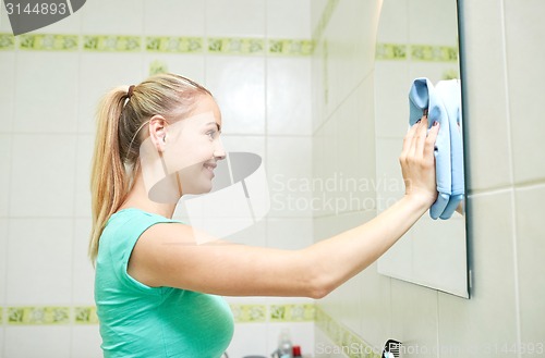 Image of happy woman cleaning mirror with rag