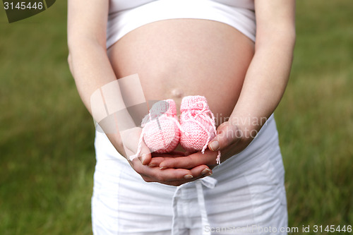 Image of Pregnant woman outdoor with pink baby shoes in her hands