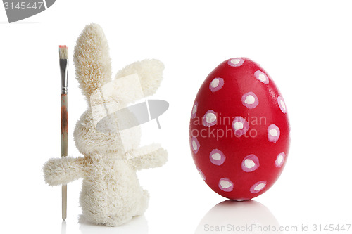 Image of Stuffed Easter bunny paints a red Easter egg