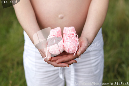 Image of Pregnant woman outdoor with pink baby shoes in her hands