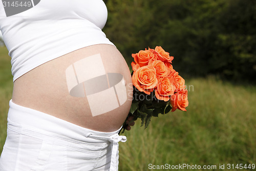 Image of Pregnant woman outdoor with orange tulips in her hands