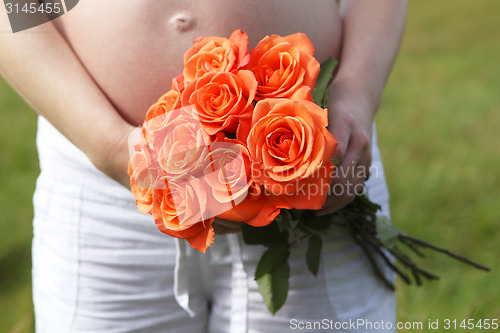 Image of Pregnant woman outdoor with orange tulips in her hands