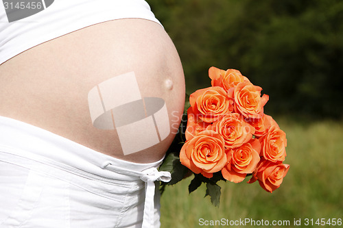 Image of Pregnant woman outdoor with orange tulips in her hands