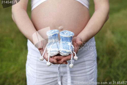 Image of Pregnant woman outdoor with blue baby shoes in her hands