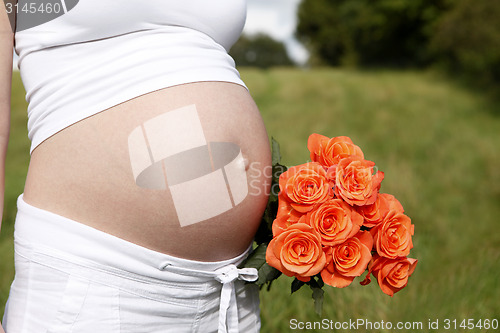 Image of Pregnant woman outdoor with orange tulips in her hands