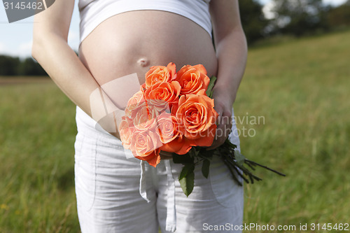 Image of Pregnant woman outdoor with orange tulips in her hands