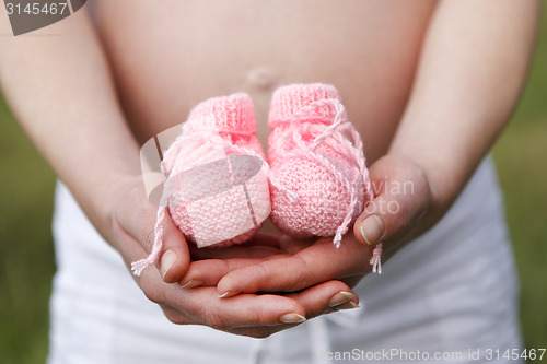 Image of Pregnant woman outdoor with pink baby shoes in her hands