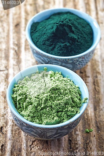 Image of bowl of spirulina algae powder and wheat sprout powder on wooden