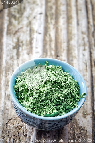 Image of bowl of wheat sprouts powder on wooden background