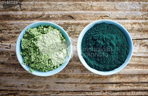 Image of bowl of spirulina algae powder and wheat sprout powder on wooden