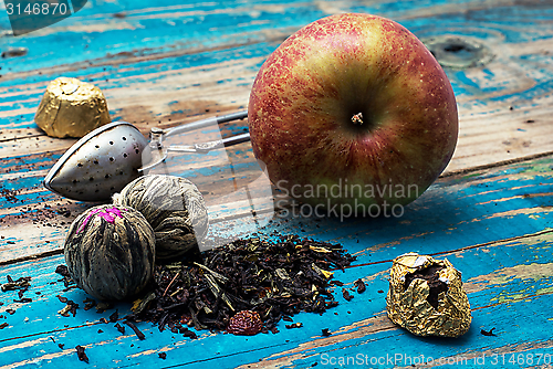 Image of tea leaves and red apple on wooden background