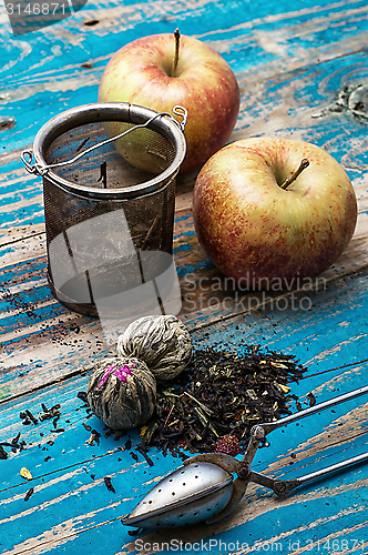 Image of tea leaves and red apple on wooden background