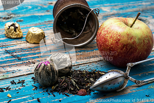 Image of tea leaves and red apple on wooden background