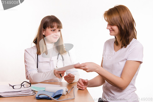 Image of Physician in the office extends to the patient a prescription or medical certificate