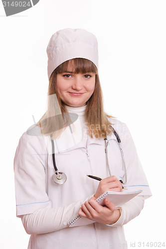 Image of Medical officer in a white coat writes in a notebook information