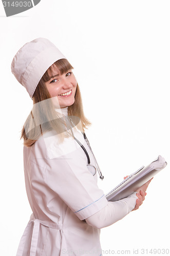 Image of Health worker in a white coat, hat stands with documents in hand and smiling