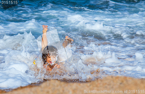 Image of Little boy laughing in the foam of waves at sea