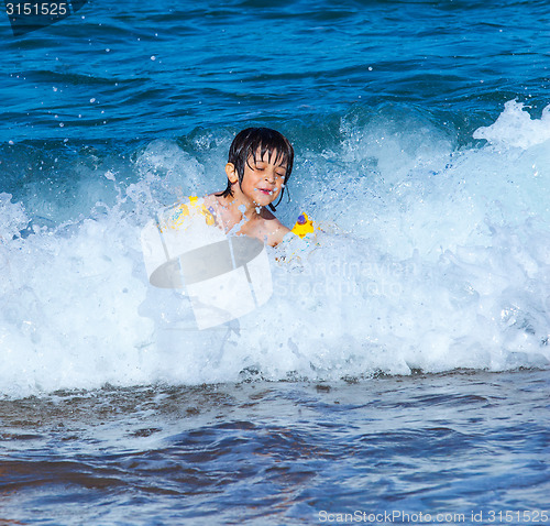 Image of Little boy laughing in the foam of waves at sea