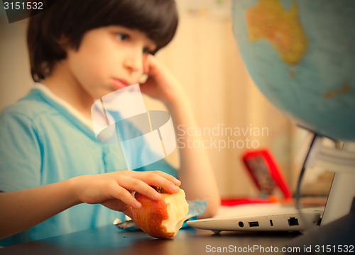 Image of boy sitting with a laptop and eating apple