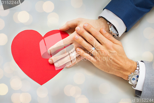 Image of close up of male gay couple hands with red heart