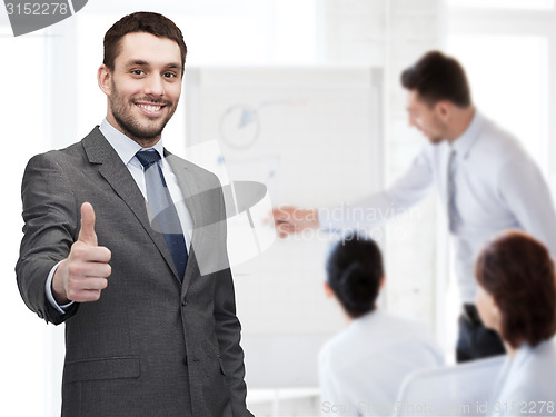 Image of handsome buisnessman showing thumbs up in office