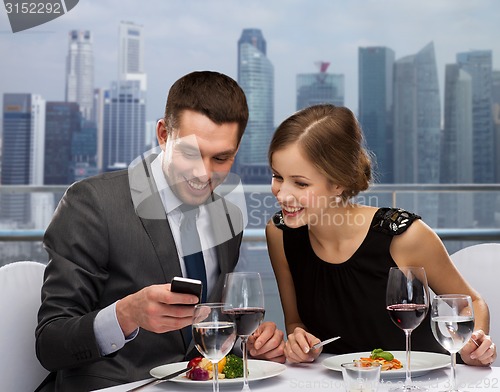 Image of smiling couple with smartphone at restaurant