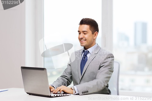 Image of happy businessman working with laptop in office