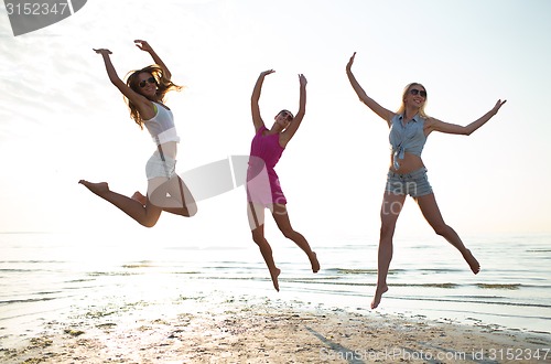 Image of happy female friends dancing and jumping on beach