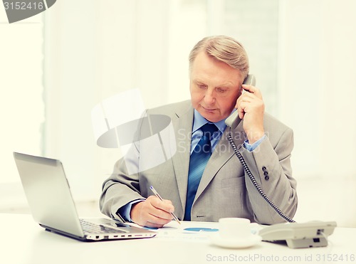 Image of busy older businessman with laptop and telephone