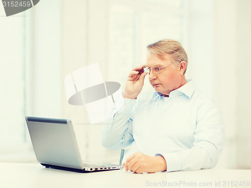 Image of old man in eyeglasses working with laptop at home