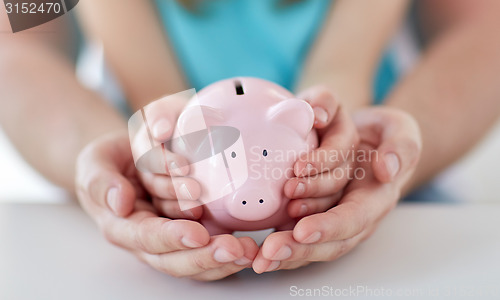 Image of close up of family hands with piggy bank