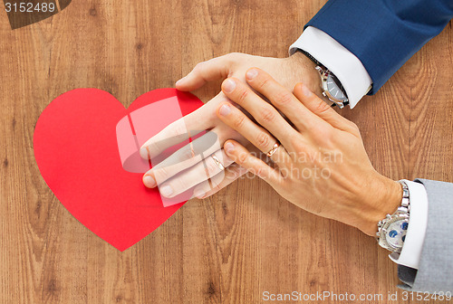 Image of close up of male gay couple hands with red heart