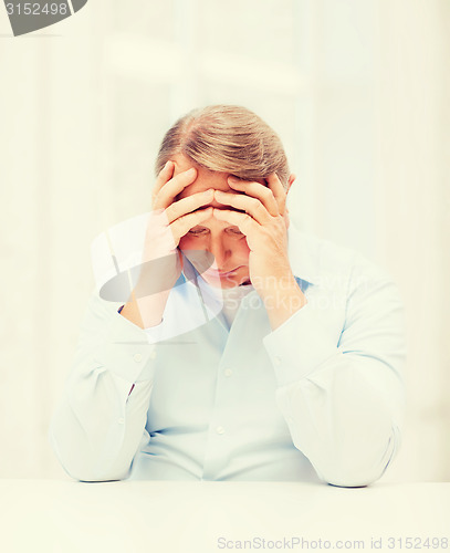 Image of stressed old man holding head at home