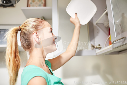 Image of happy woman putting plate to kitchen cabinet