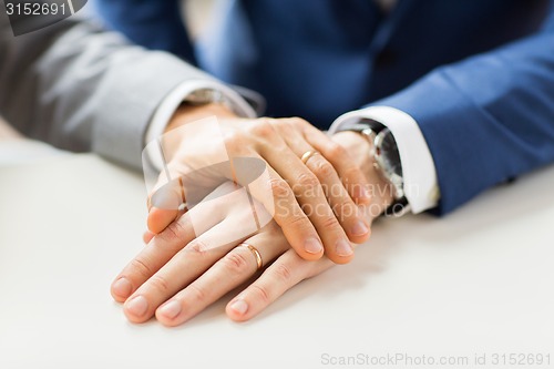 Image of close up of gay couple hands with wedding rings on