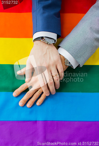 Image of close up of male gay couple hands on rainbow flag