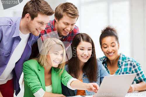 Image of smiling students looking at laptop at school