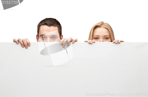 Image of happy couple hiding behind big white blank board