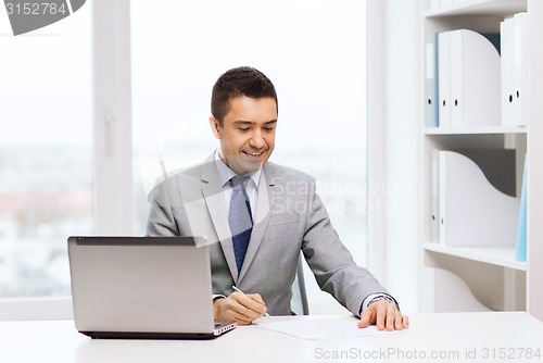 Image of smiling businessman with laptop and papers