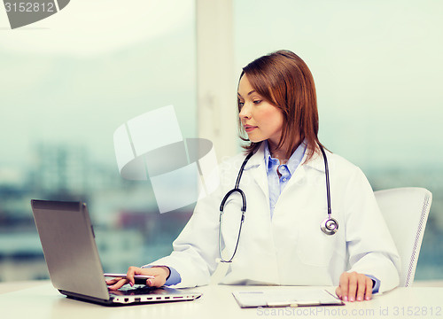 Image of busy doctor with laptop computer and clipboard