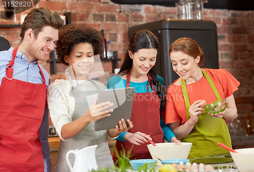 Image of happy friends with tablet pc cooking in kitchen